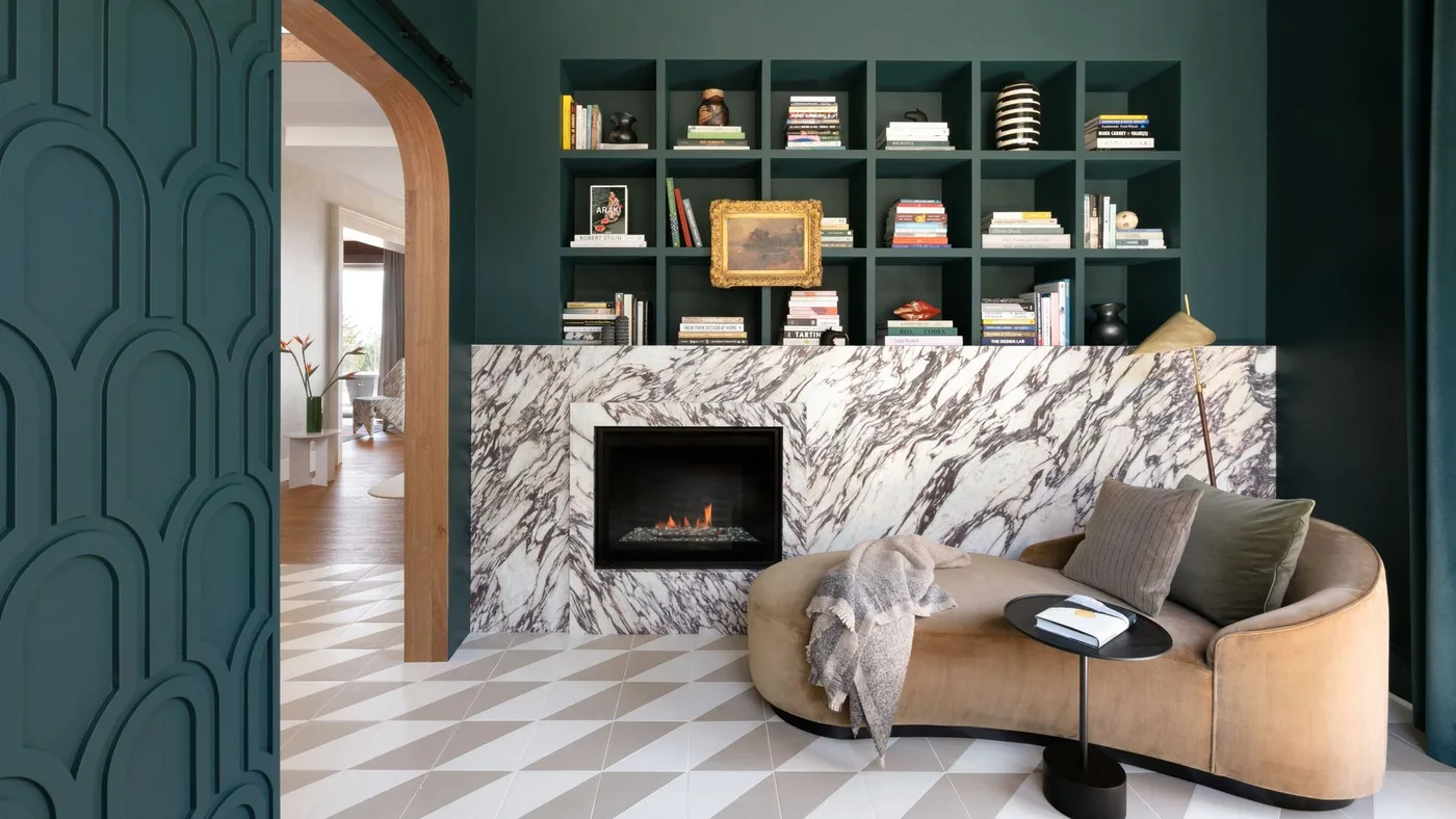 Deep green cubby shelves above broad white and dark veined fireplace face with curved pale sofa