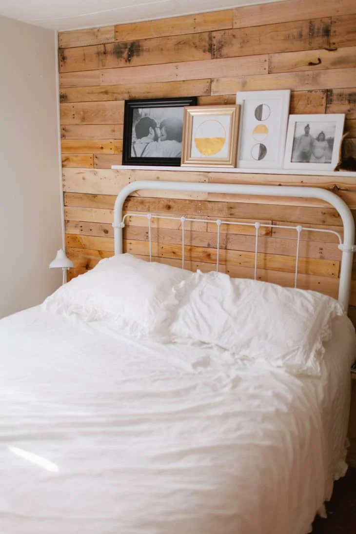 A white metal bed and plain white bedding against a horizontal timber board accent wall