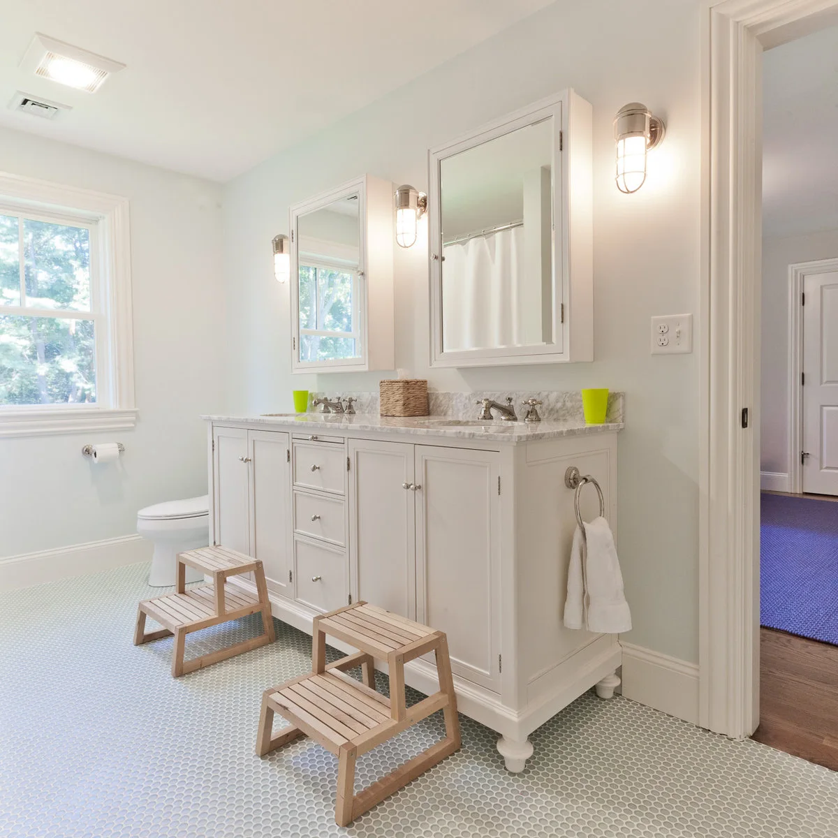 A round towel ring is mounted on the end of a white double vanity beside a doorway, with two step stools in front.