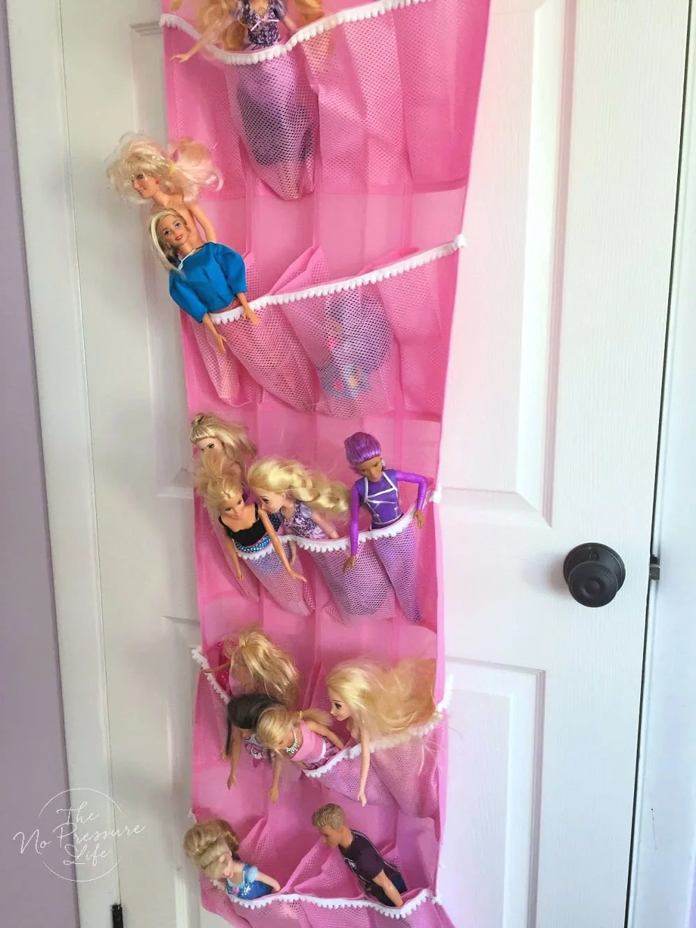 Pink hanging mesh pocket organizer on a white door holding several fashion dolls.
