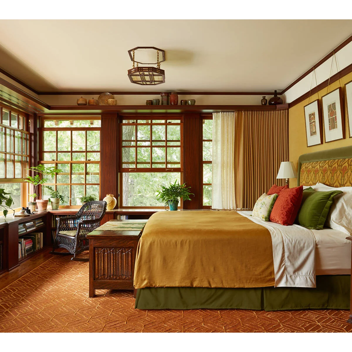 Bedroom with broad brown window trim, ochre bedding, olive accents and a wooden chest at the foot of the bed.