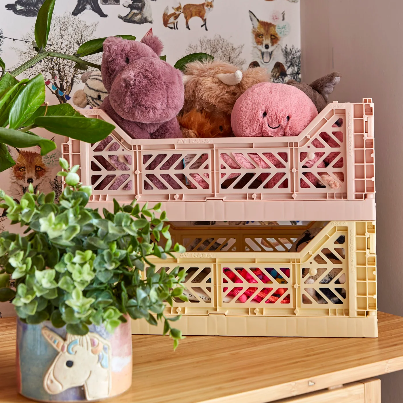 Pink crate filled with stuffed animals above a yellow crate containing more soft toys and a book