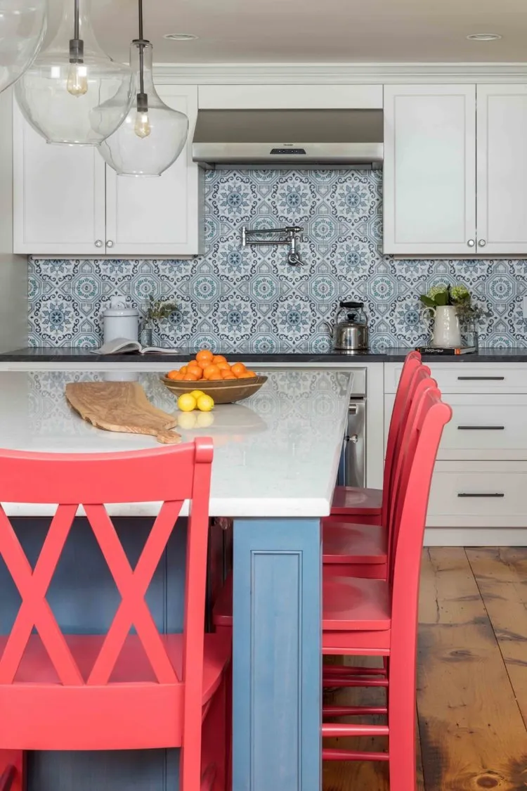 A pale blue island stands beside white cabinets and bright red chairs