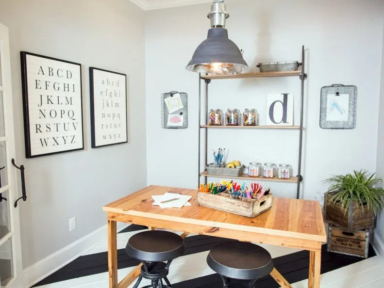 Country craft workspace with wood table, dark round stools, pipe-framed shelves, jars of supplies and dome pendant