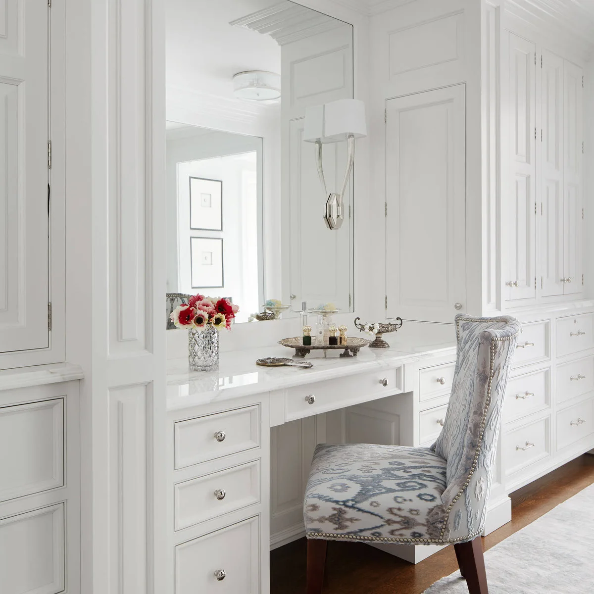 A white fitted vanity with drawers and a large wall mirror sits within a run of bedroom cabinetry