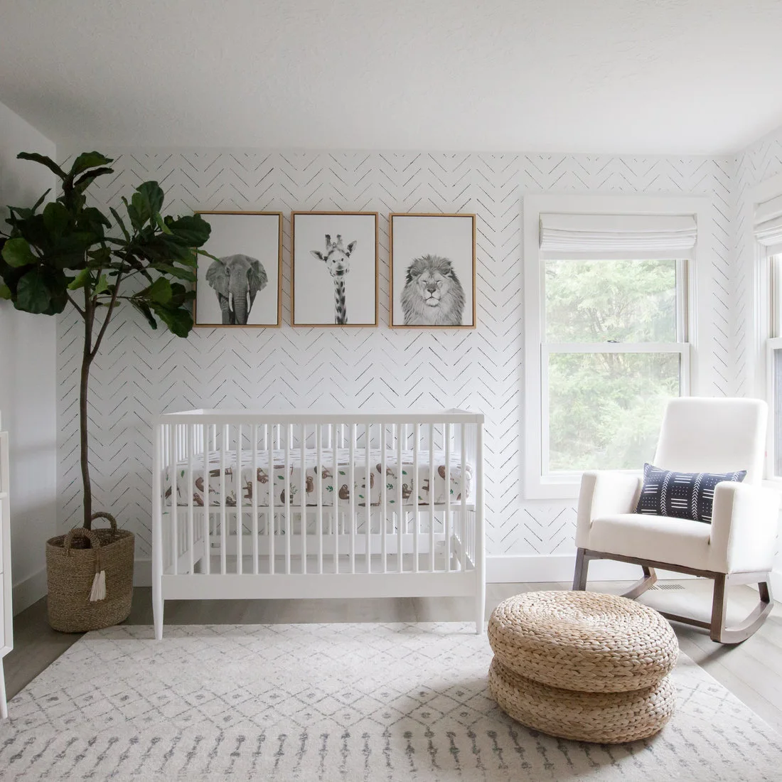 Small nursery with a white crib, pale rocking chair, woven footstool and three framed animal pictures