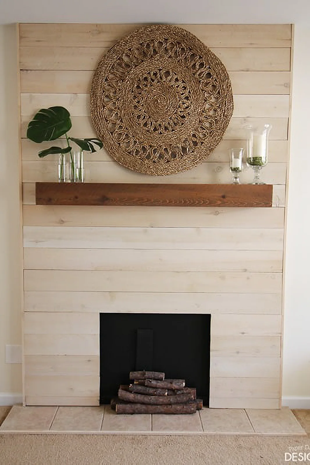 A pale wood shiplap feature has a simple wood shelf, dark decorative opening with stacked logs and a large round woven wall piece.