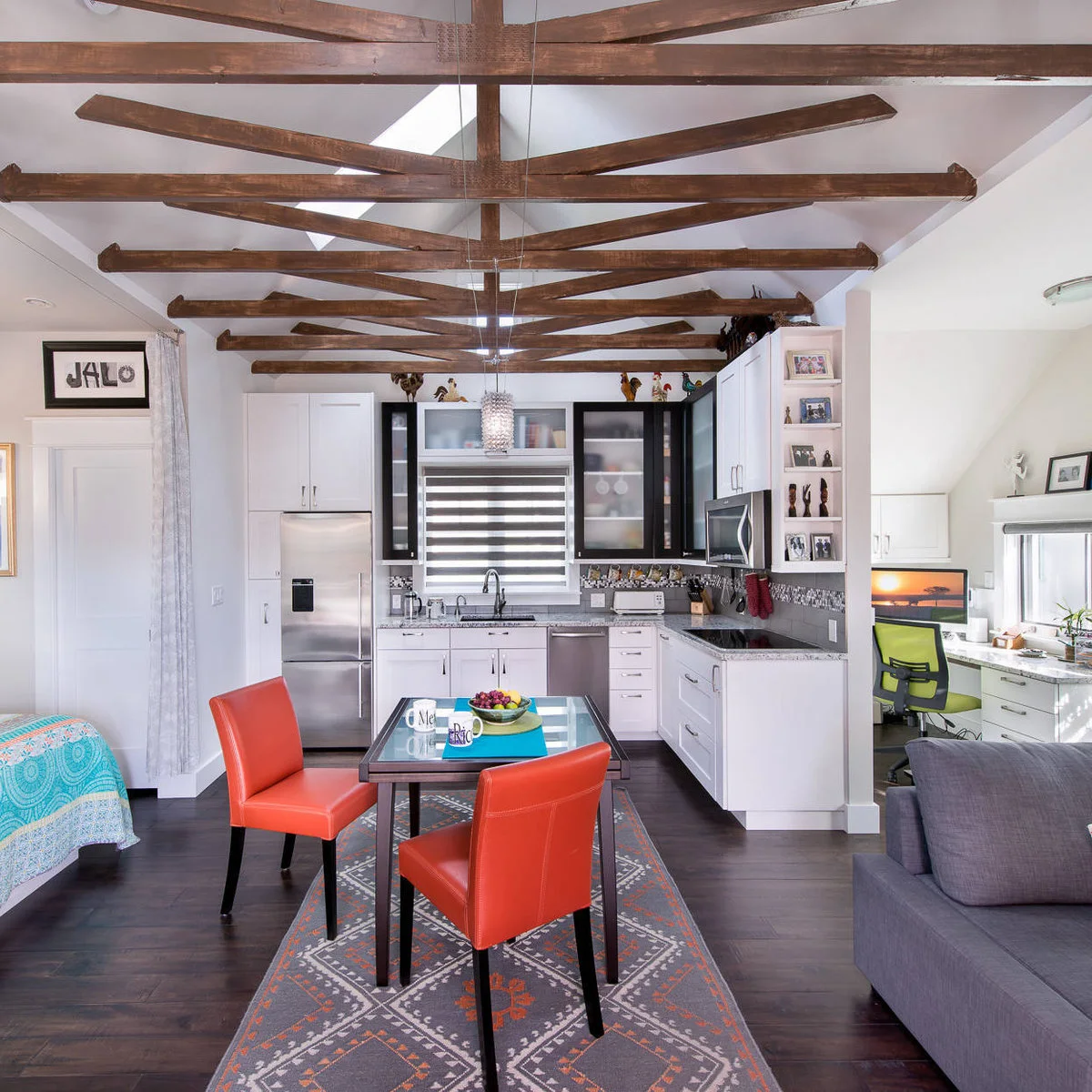 Compact open kitchen with exposed beams and a small glass dining table with red chairs