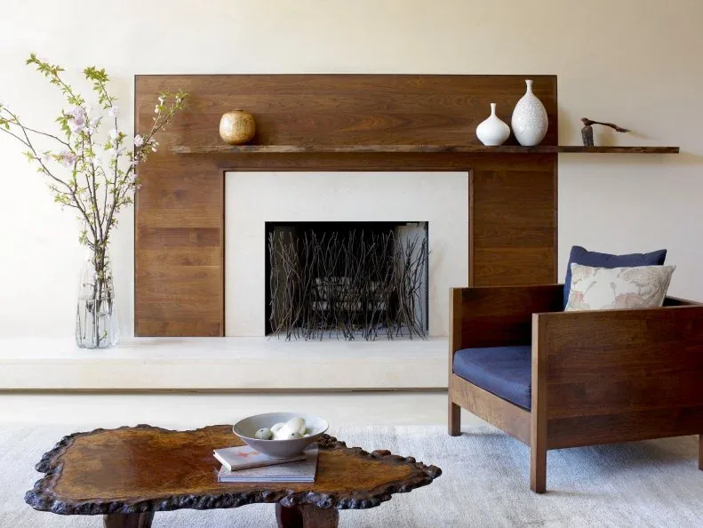 Wood-surrounded fireplace with long pale hearth, tall flower vase and blue-cushioned wood chair