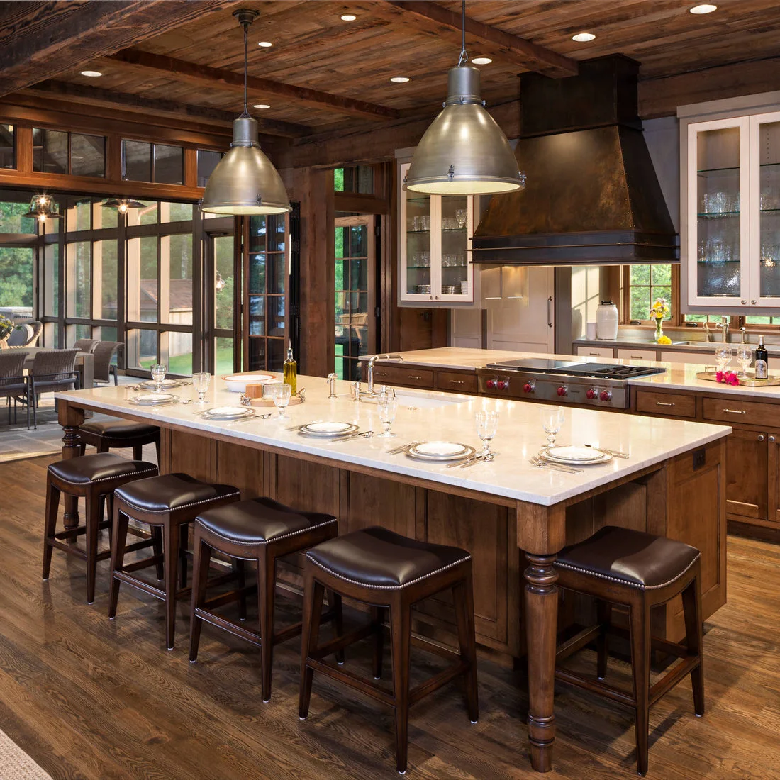A wood island with pale counter beneath metal pendants beside white glass front cabinets