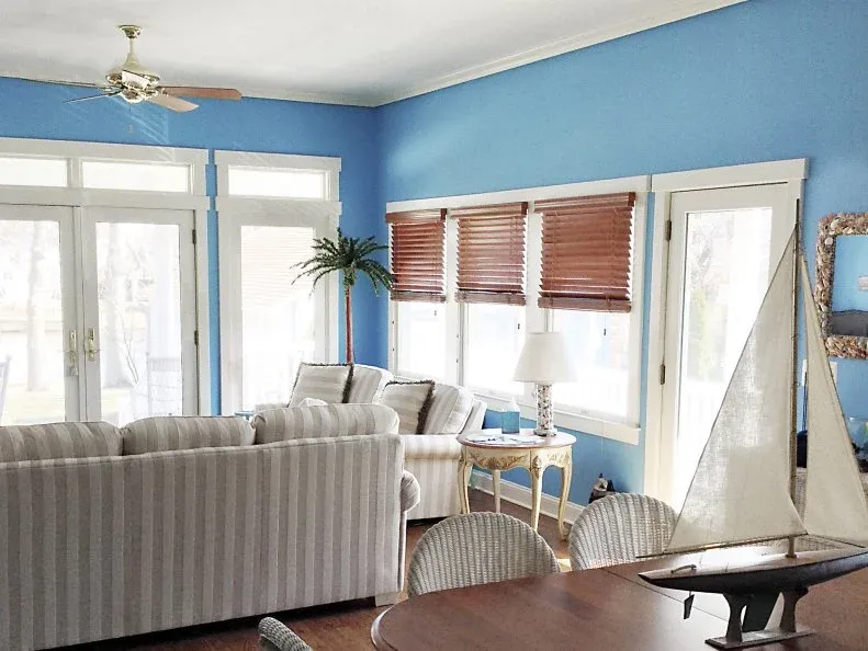 Blue-walled living room with broad white window trim, striped seating and a model sailboat in the foreground.