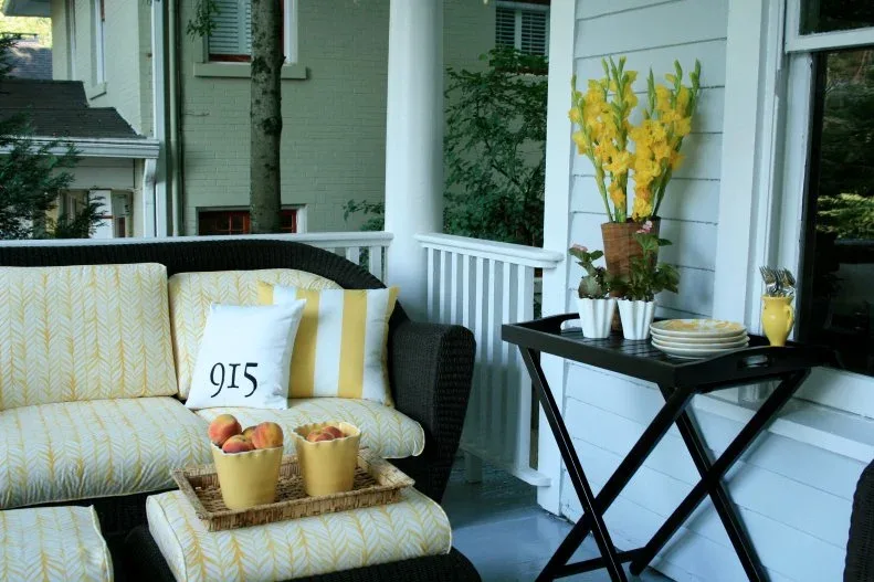 Black woven porch sofa and matching ottoman with yellow patterned cushions beside a black tray table