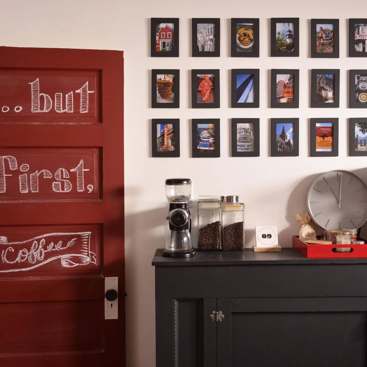 Dark sideboard with coffee grinder, clear bean jars and a red tray beneath small framed pictures