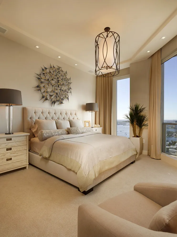 A pale tufted bed sits beneath a decorative pendant in a warm beige room