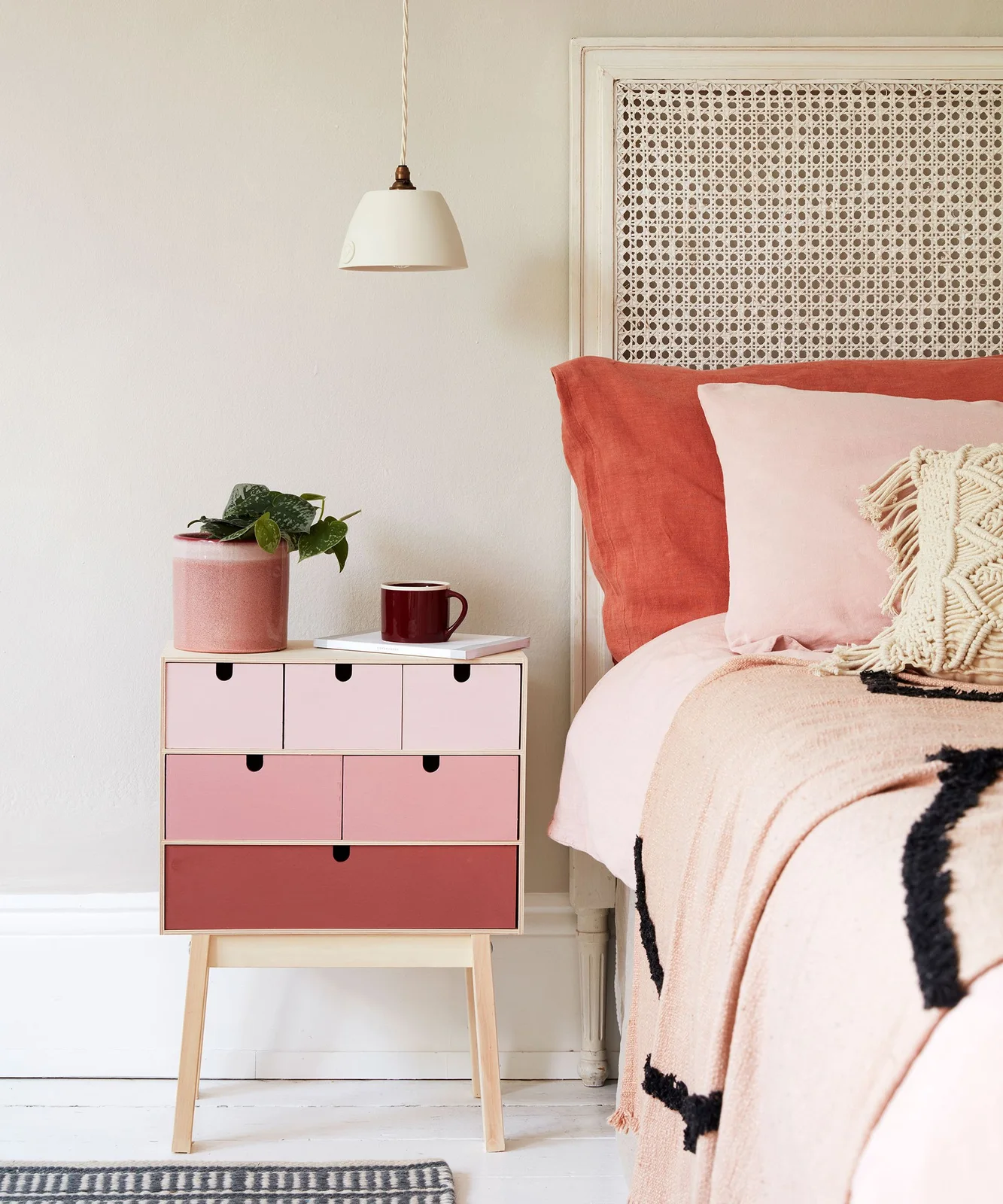 Pink graduated small-drawer bedside cabinet on a light wooden base beside a bed