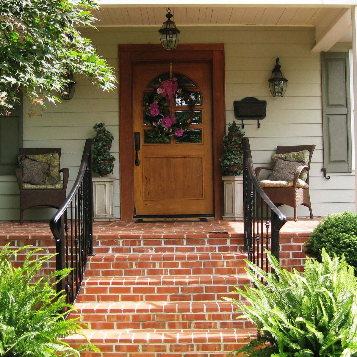 Brick front porch with two woven-looking chairs, planters and curved dark handrails