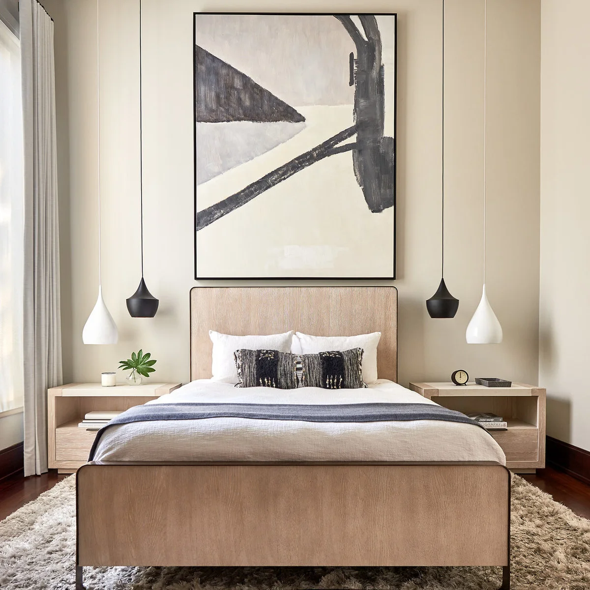 Tall monochrome abstract painting above a pale headboard between paired black and white pendant lights.