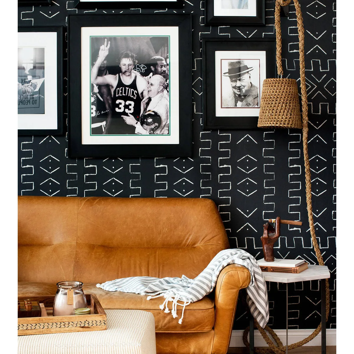 Tan sofa against black patterned wall covering with framed photographs and small side table