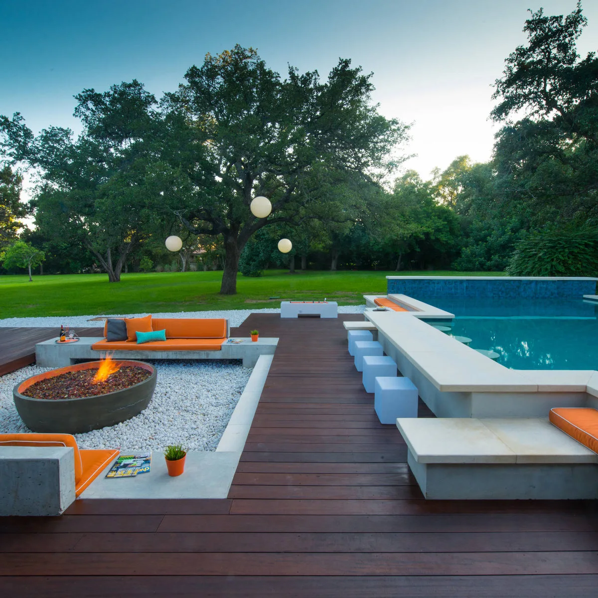 Long pale counter beside a pool with light blue cube stools, orange built-in lounge cushions and timber decking