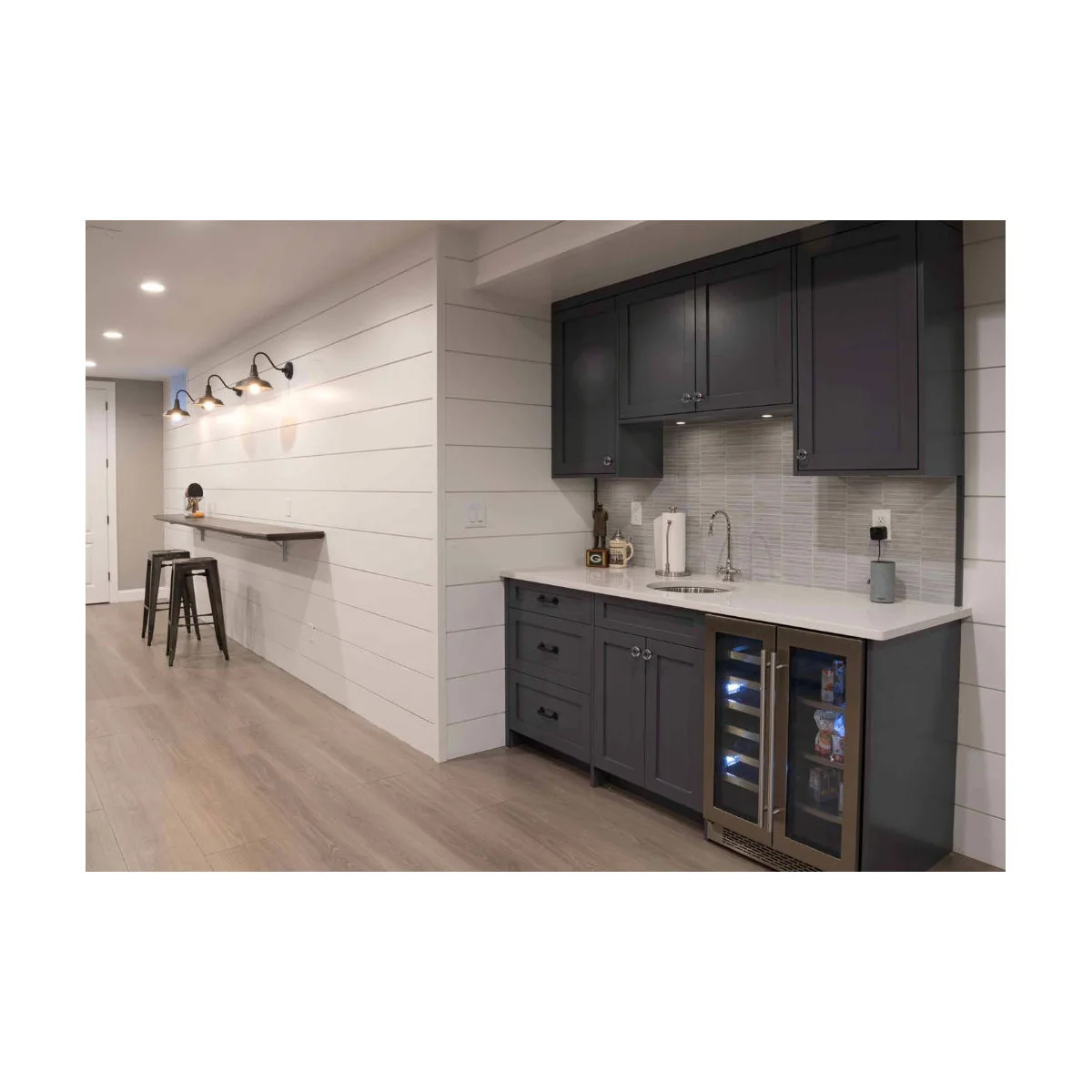 Small dark basement bar niche with sink, upper cupboards and beverage cooler