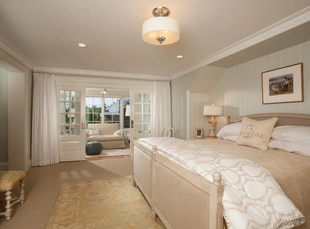 A beige bed and pale carpet sit beneath a light ceiling beside long curtains