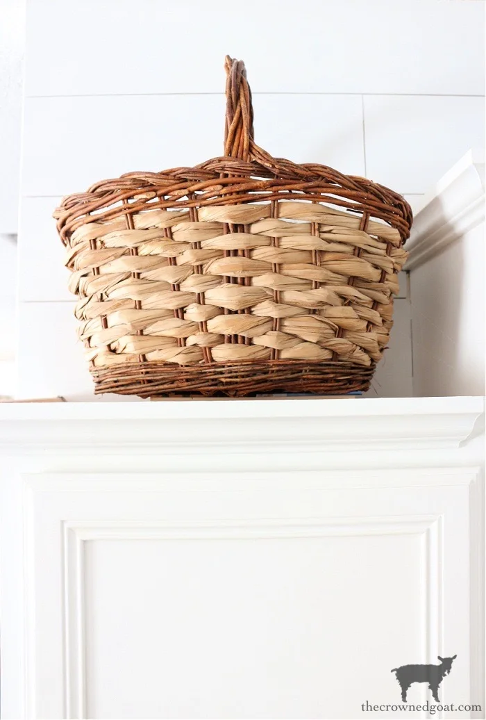 Single woven handled basket above a white kitchen cabinet against pale horizontal wall boards.