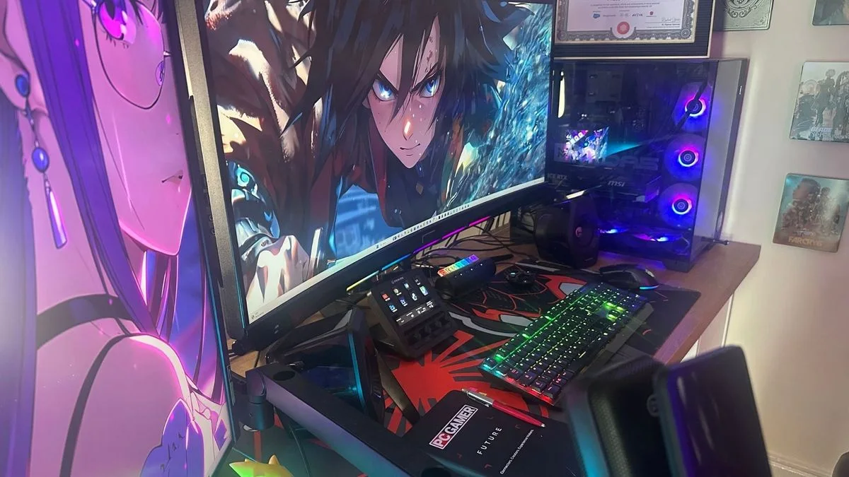 A gaming desk with two monitors, an illuminated tower, a colorful keyboard and framed certificates and artwork on the adjacent wall.