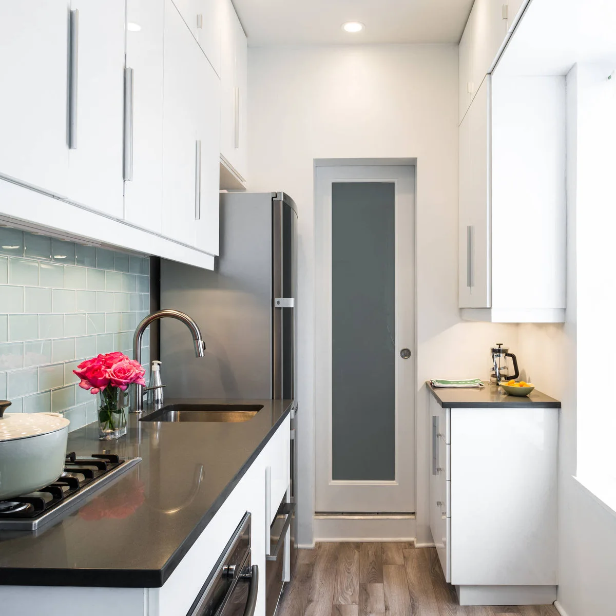 White galley kitchen with a full-depth sink run opposite a shorter narrow counter and sliding door