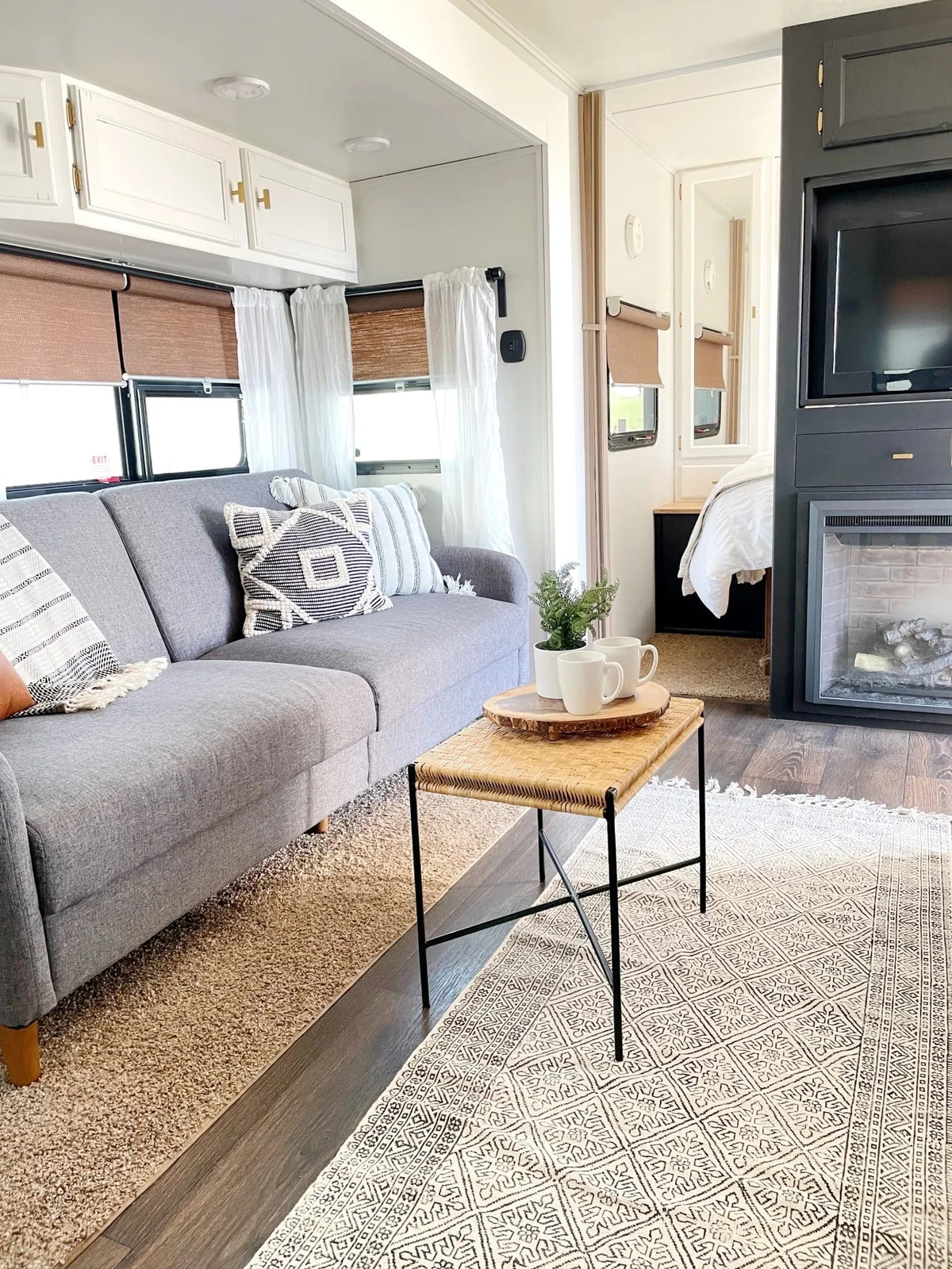 RV seating area with a gray sofa, patterned cushions and a narrow woven-top table on black legs.