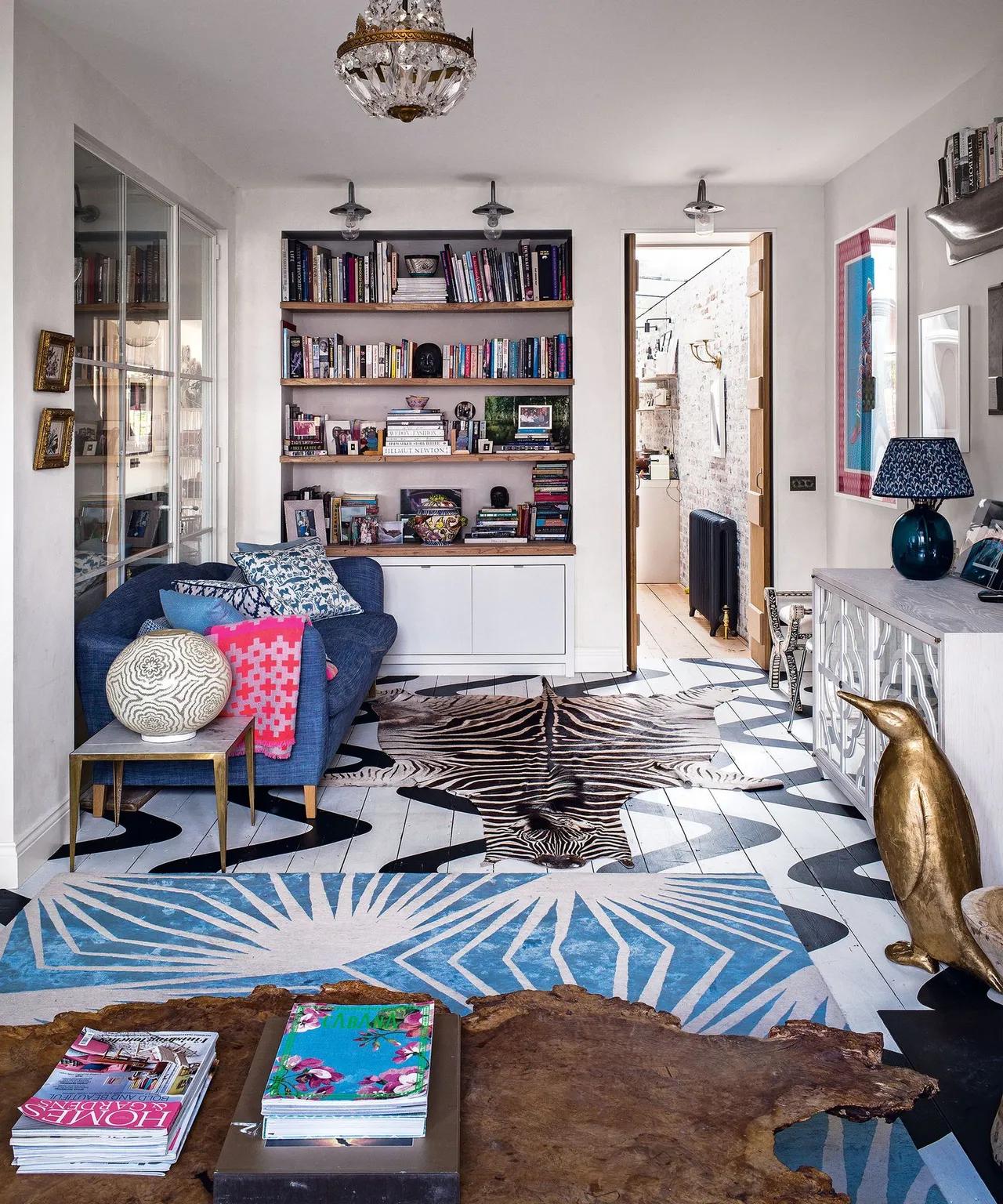 A bright blue patterned rug runs between varied furniture and pale shelving.