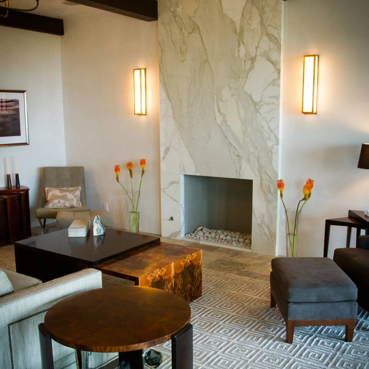 Two tall rectangular glowing wall lights flank a broad pale veined fireplace against warm neutral walls.