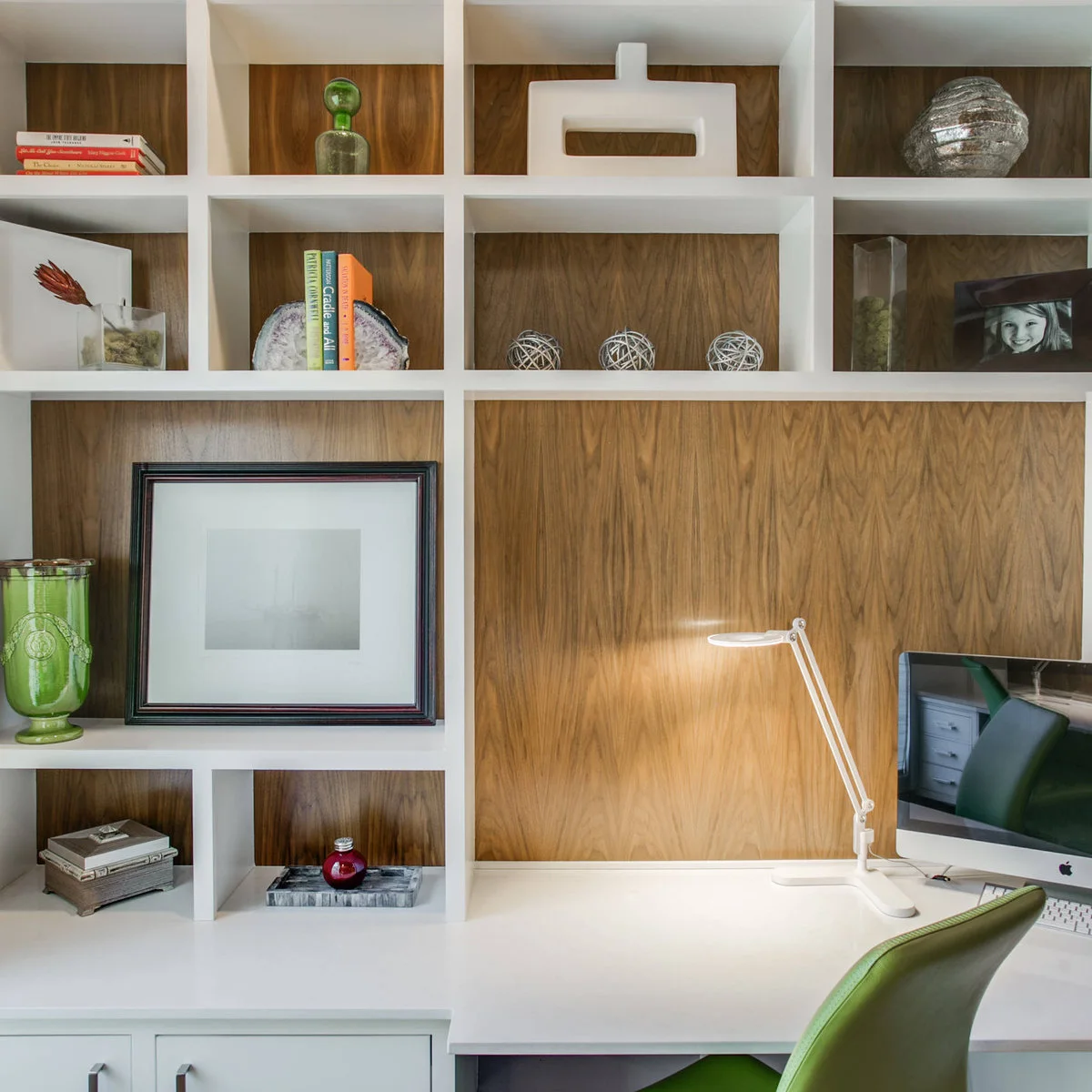 White desk integrated with open cubby shelves, wood backing, green chair and slim white task lamp