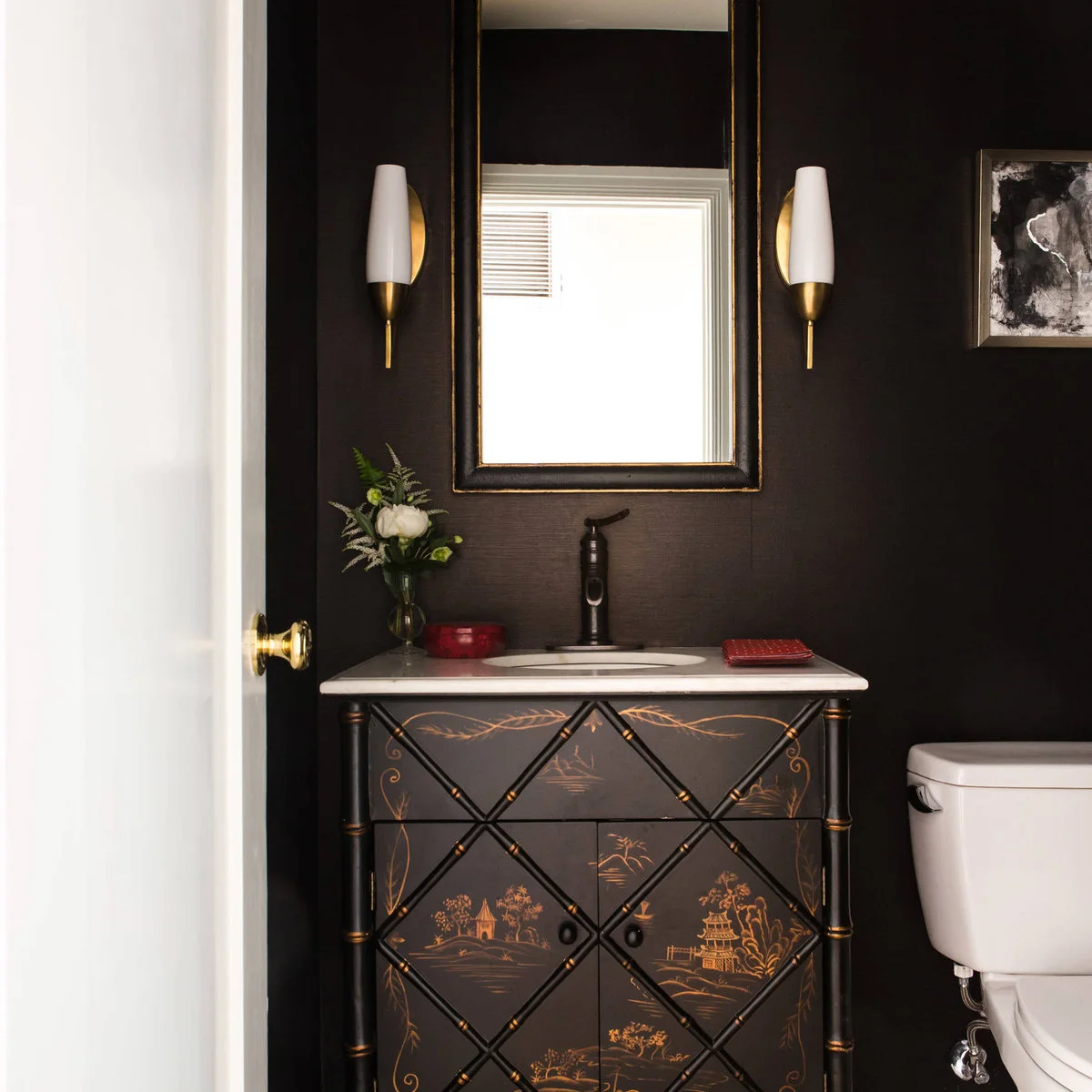 Two pale tapered sconces with warm metal backplates flank a narrow mirror above a patterned powder room cabinet.