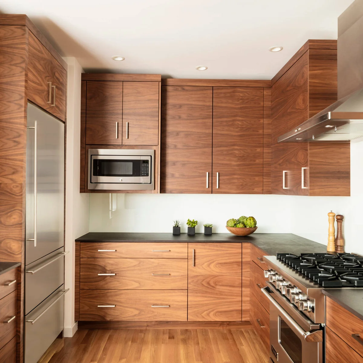 A compact kitchen with strongly grained wood cabinet fronts, simple metal handles and dark counters beside stainless appliances.