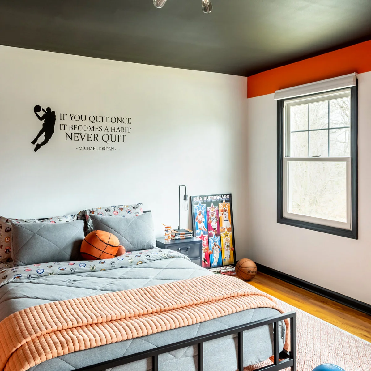 Teen basketball bedroom with gray bedding, an orange accent band and dark window trim