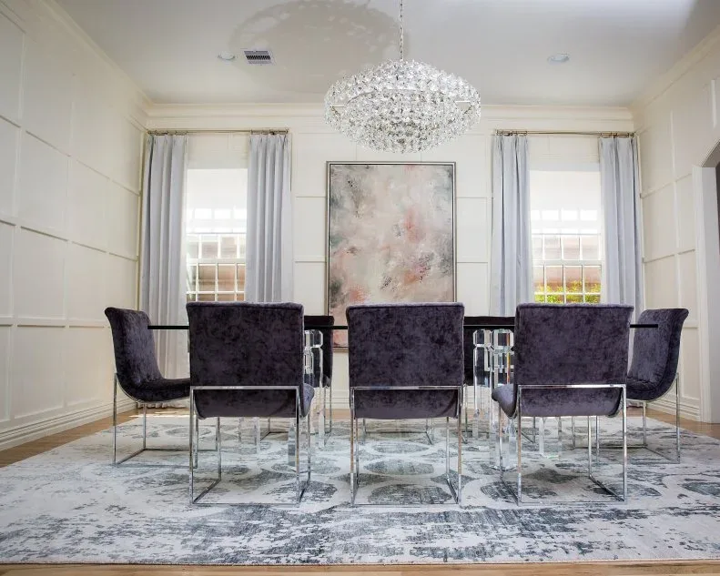 Purple dining chairs on slim bright metal frames beneath a clustered clear crystal chandelier in a pale room.