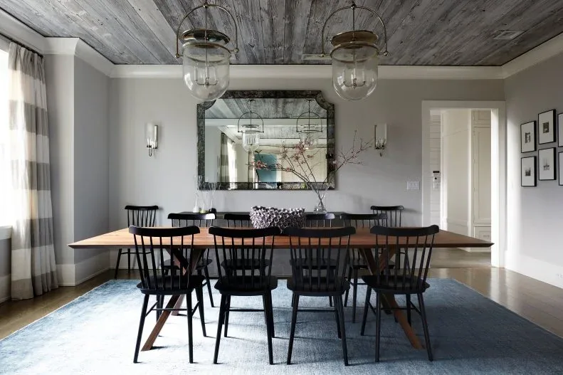 Gray dining room with black spindle chairs, a wood table, two large glass pendants, broad striped curtains and a framed mirror