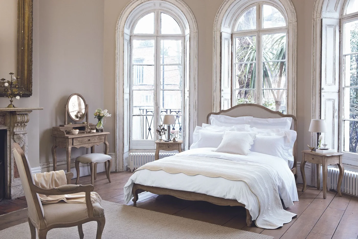 A small timber dressing table and matching stool sit beside a bed with a similarly curved timber frame