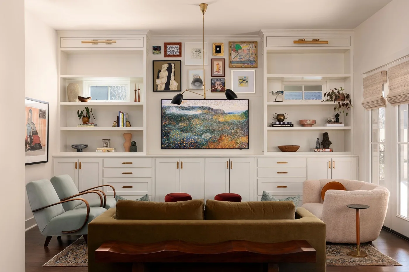 An art-displaying television sits between pale built-in shelves and drawers behind a green sofa, light chairs and small framed pictures