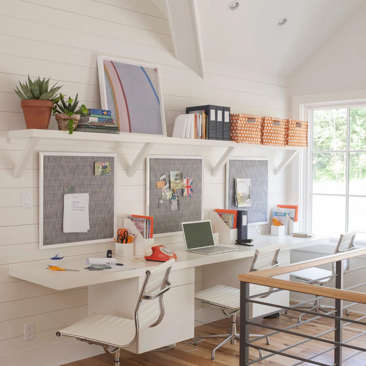 Long white shared desk with three chairs, separate framed noticeboards and orange storage boxes above