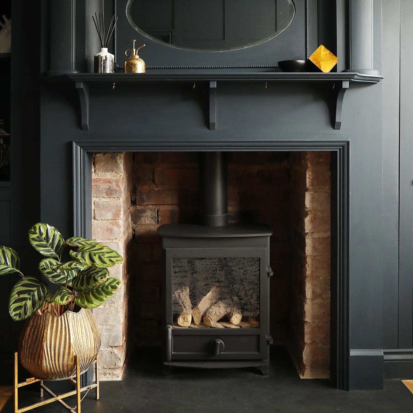 Black fireplace wall and mantel with oval mirror, small metallic objects and stove in brick recess
