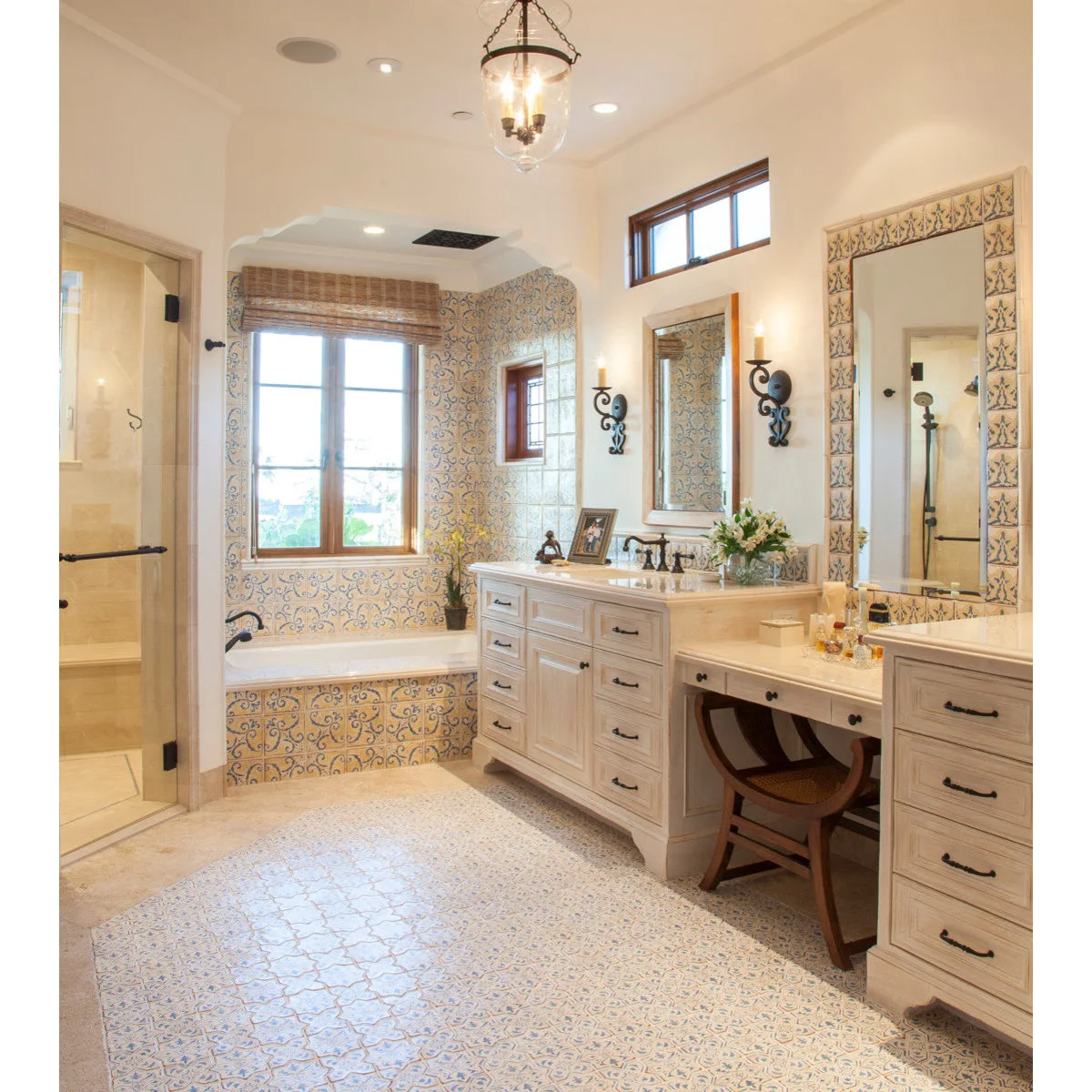 Pale bathroom with blue-and-yellow tiles around the bath alcove and mirror, plus patterned flooring