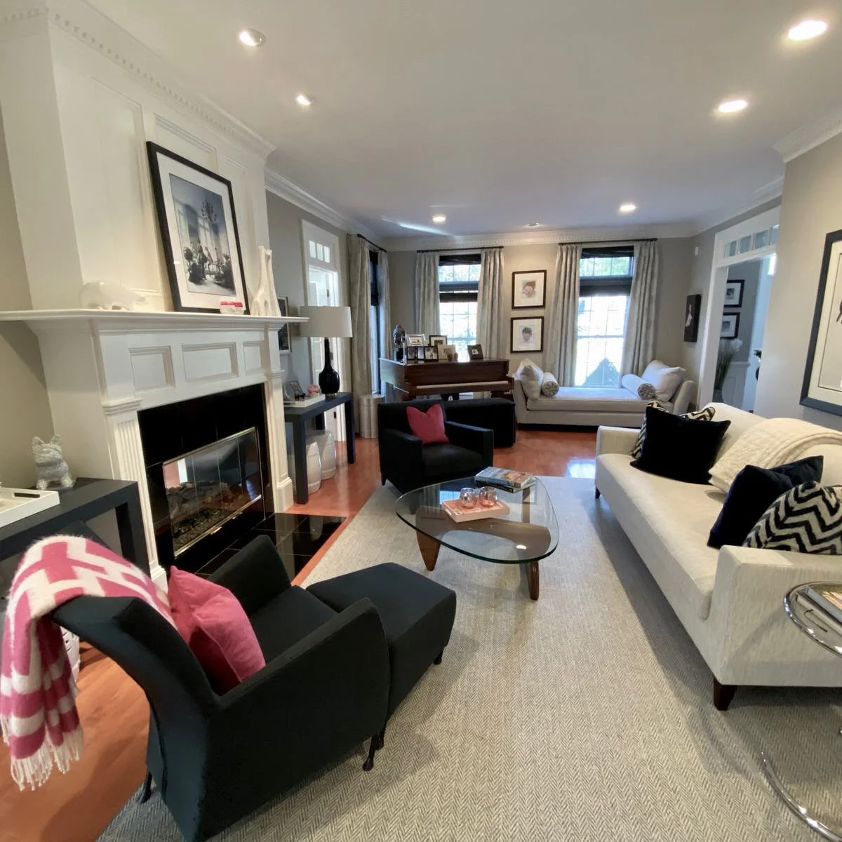 Long gray living room with a white sofa, two black chairs, glass table, piano and pale chaise near windows