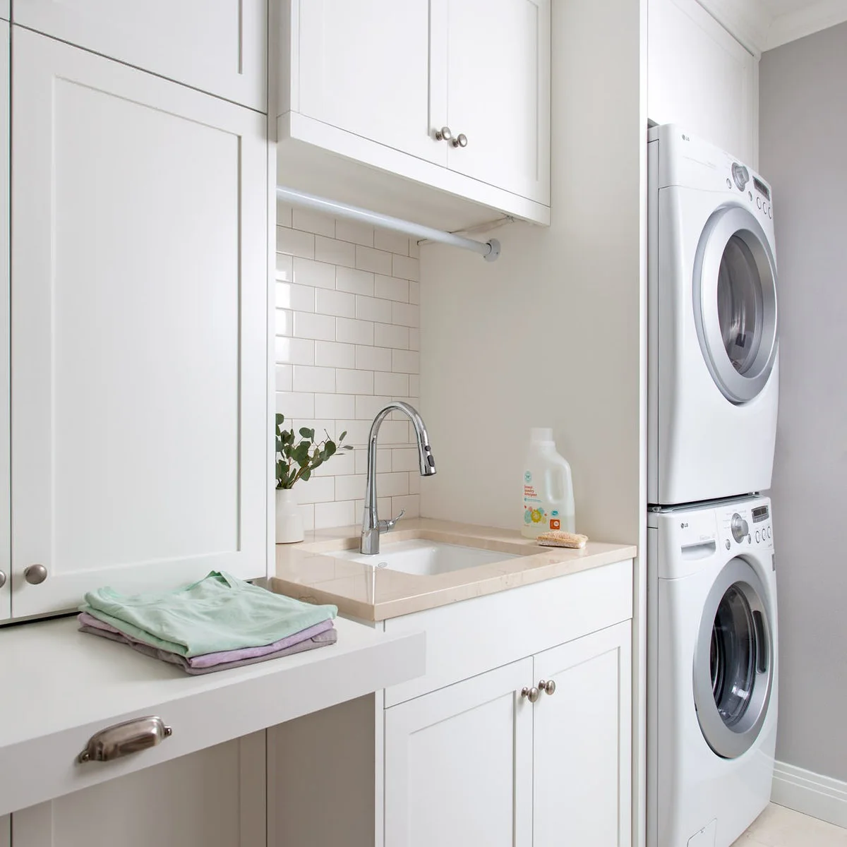 Stacked white laundry appliances beside a white sink cabinet and counter with a hanging rail above