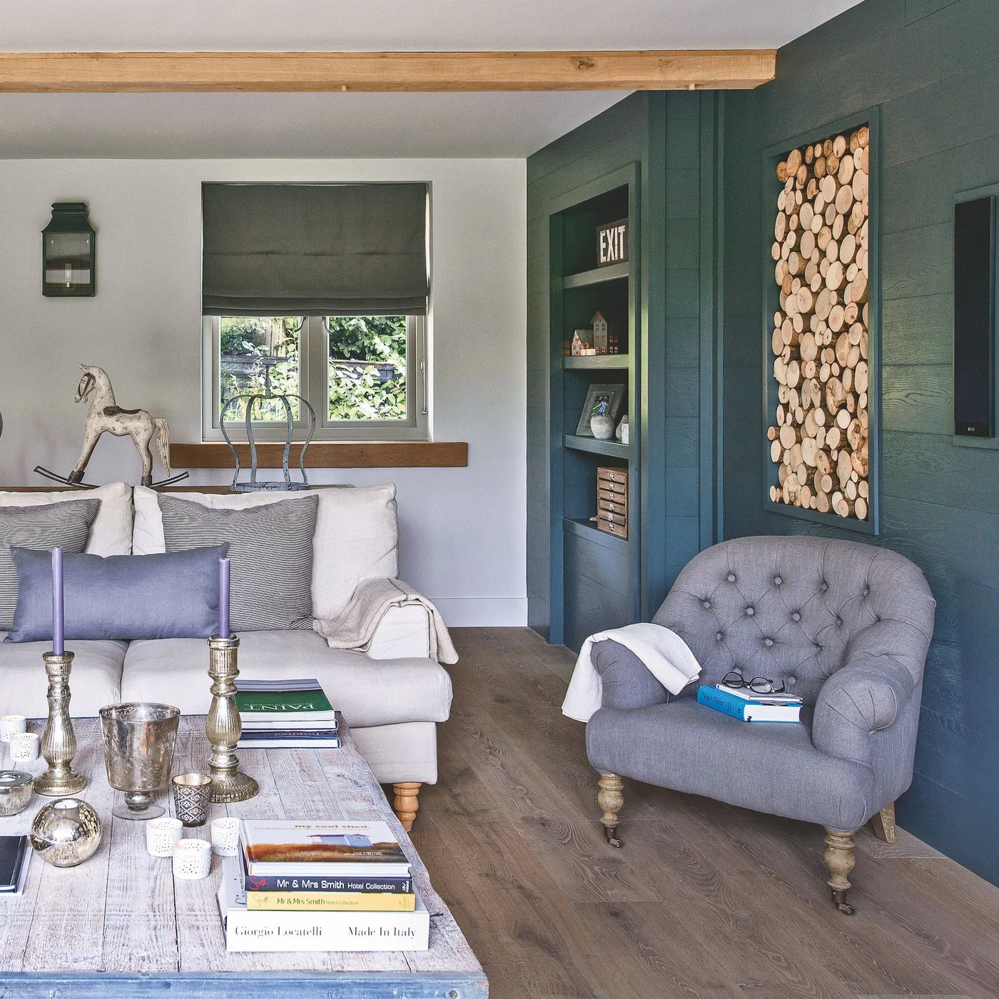 A pale sofa and gray chair sit beside a deep green boarded wall, warm wood trim and a framed arrangement of log ends.