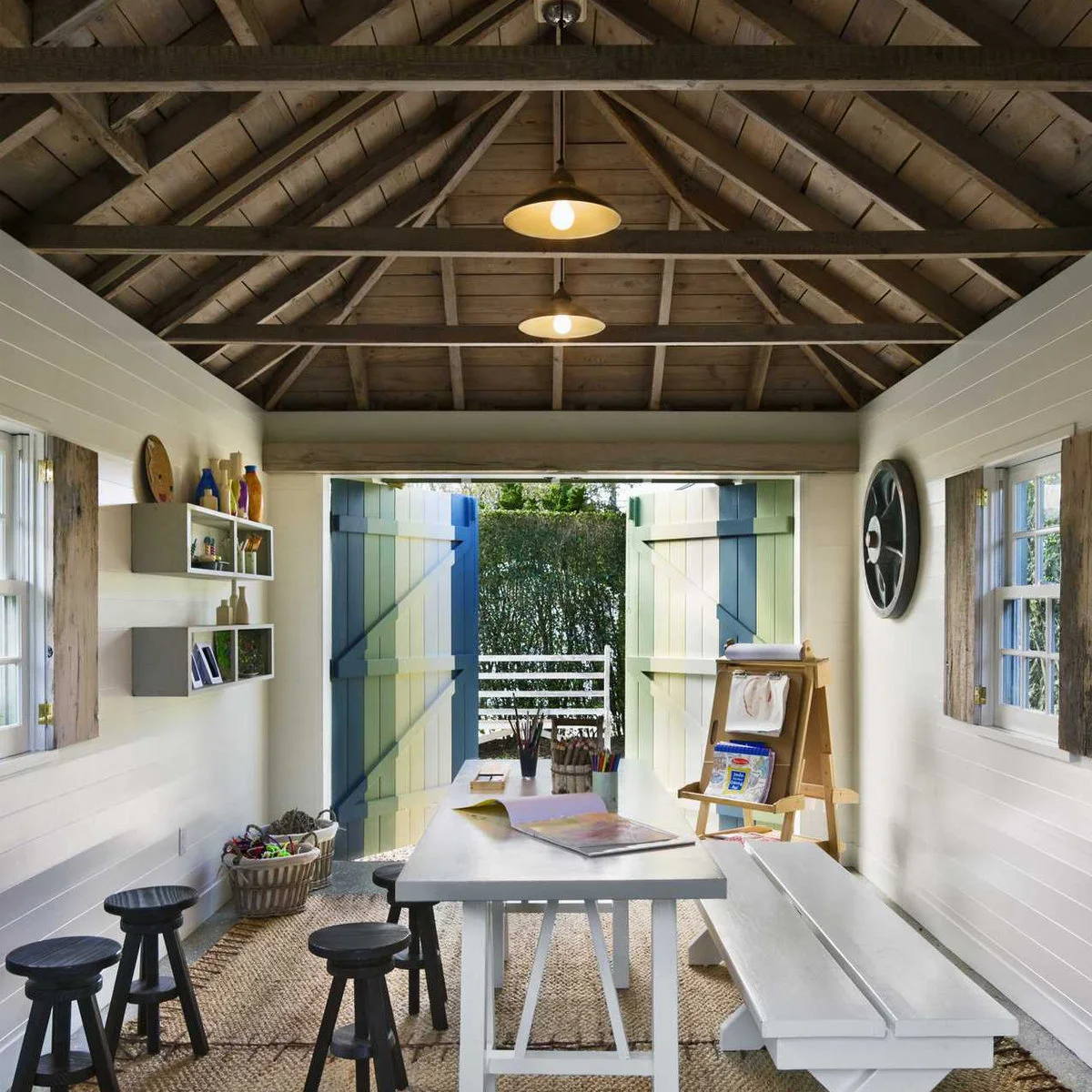 Exposed pale timber ceiling above a white worktable and dark stools in a small studio