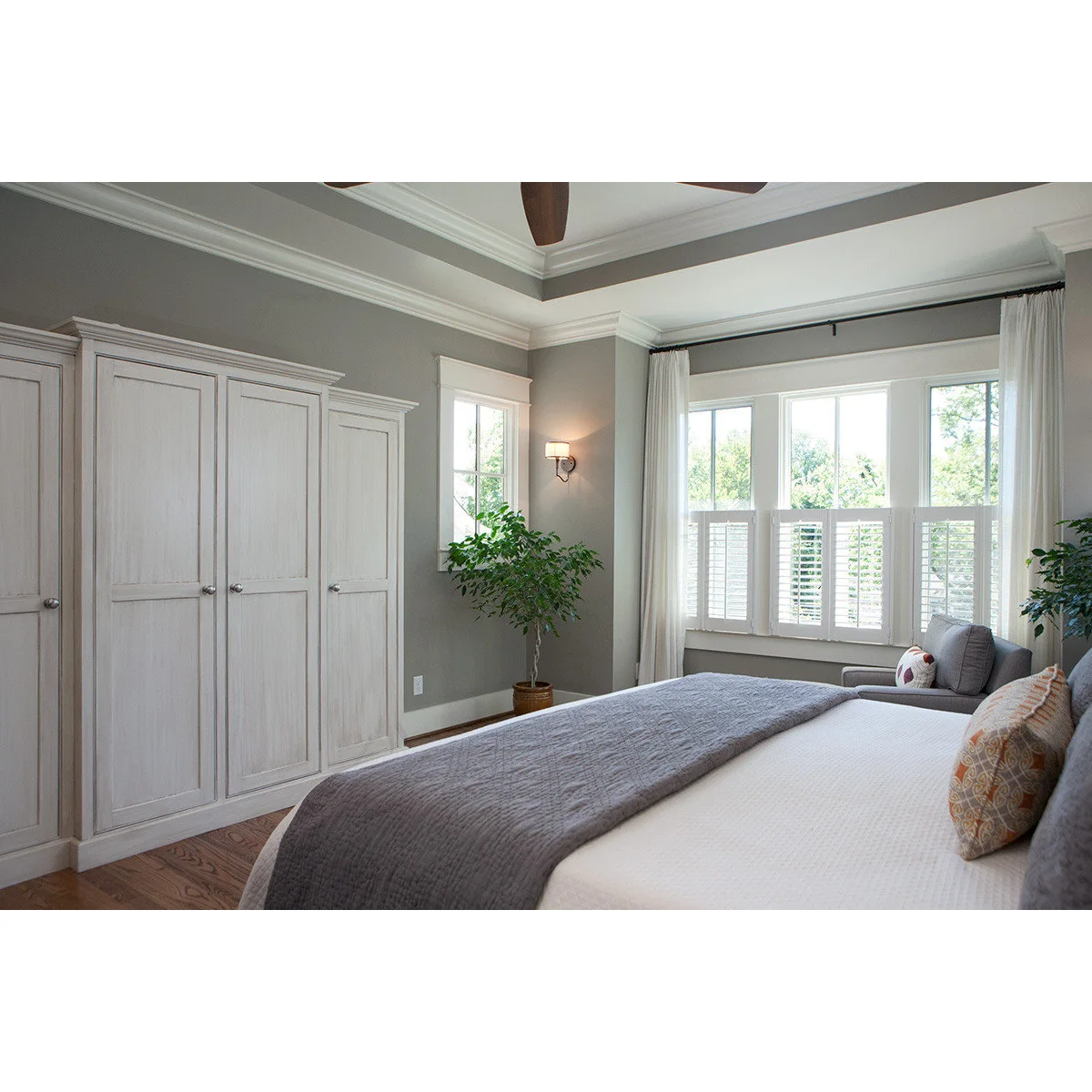 Grey bedroom walls beside pale built-in wardrobes, white bedding and a grey throw