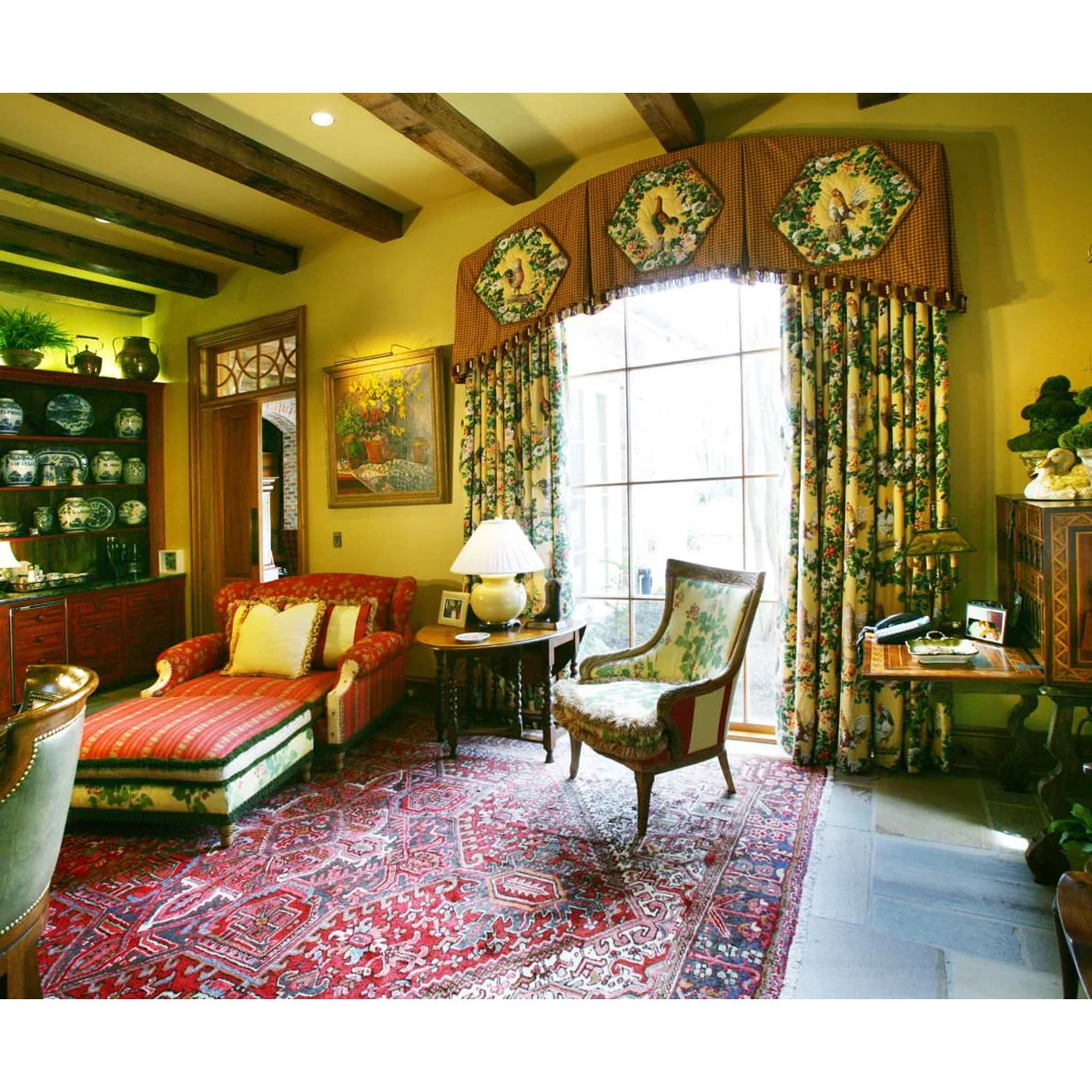 Traditional yellow sitting room with a red chaise, floral curtains, patterned rug and dark wood display storage