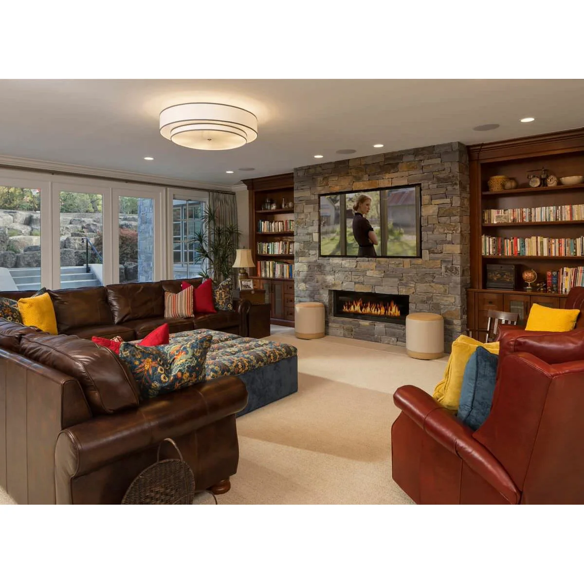 A television above a stone-textured fireplace between full wood bookshelves, with a brown sectional and colorful cushions.