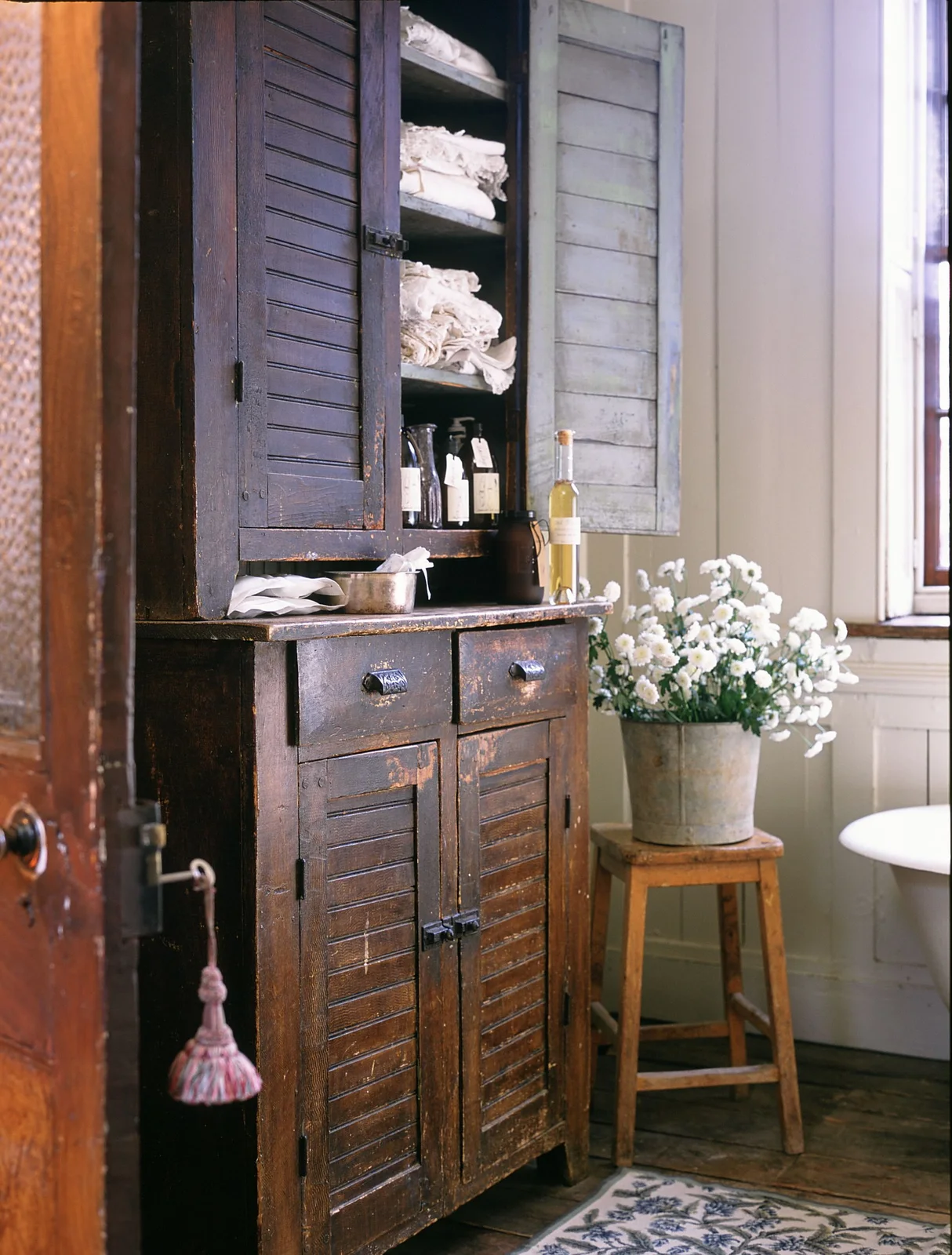 Dark rustic cupboard with pale folded linens above bottles and a lower pair of paneled doors